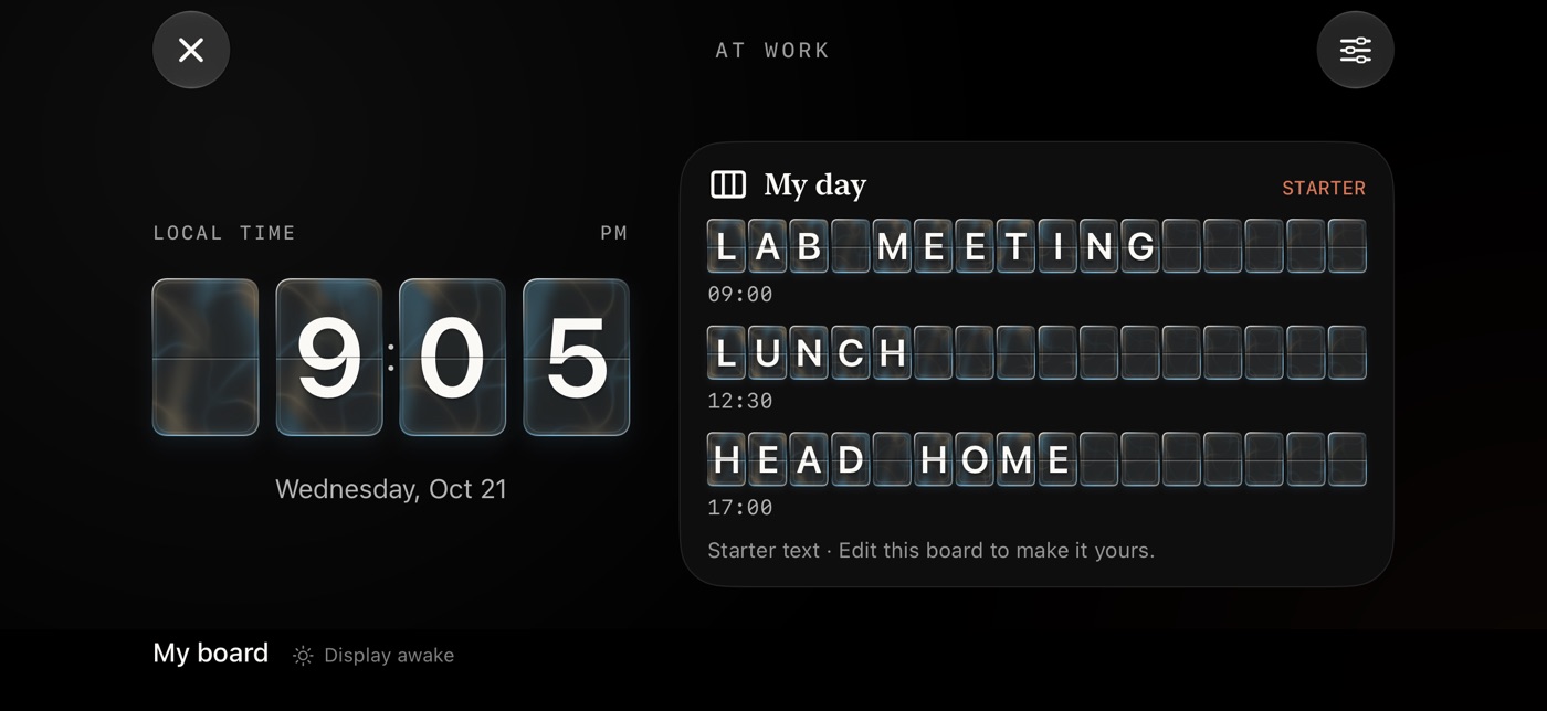 The At work display in landscape on a dark screen. A large split-flap clock reads 9:05 PM on the left. On the right, a board titled My day shows three lines of flap tiles: Lab meeting 09:00, Lunch 12:30, Head home 17:00, marked as starter text.